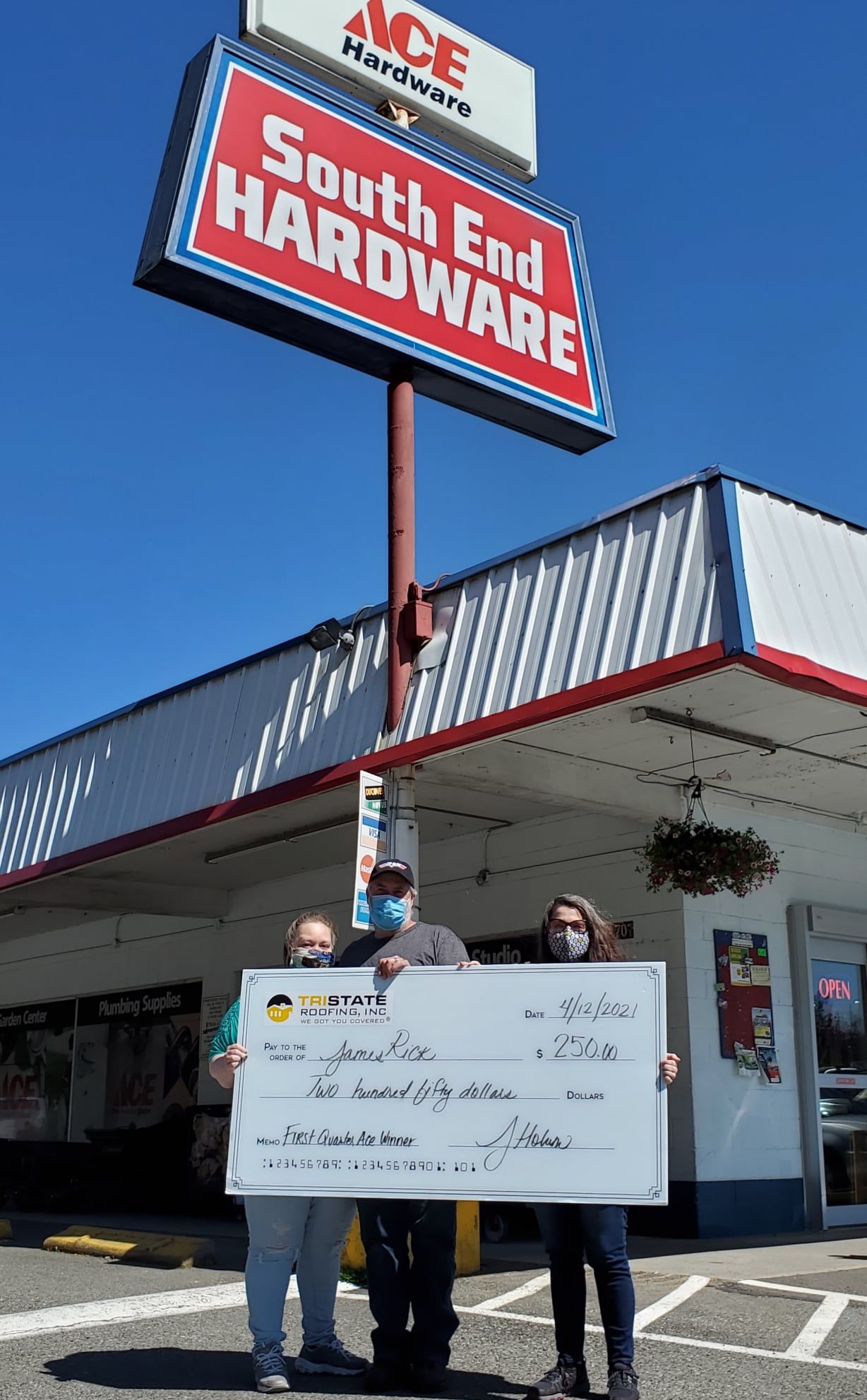 A group of people holding a check in front of a hardware store.