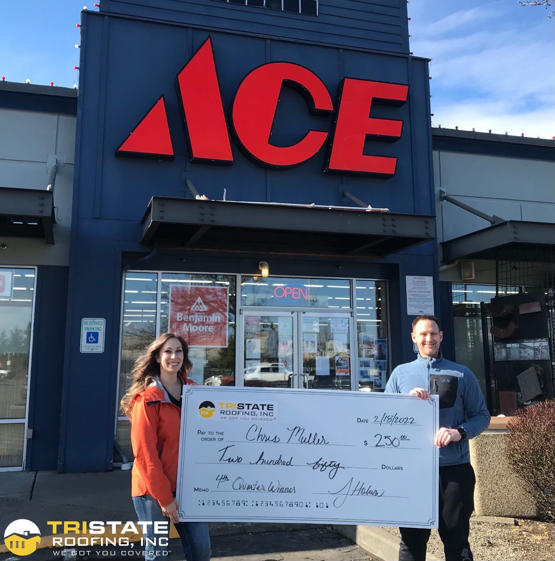 Two people holding a check in front of an ace hardware store