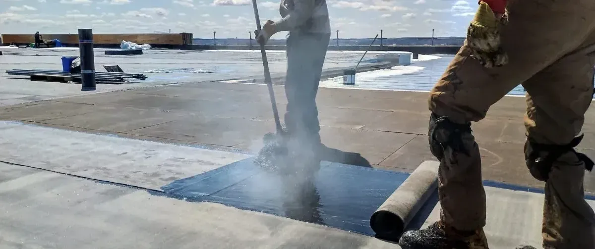Crew applying layers of asphalt and roofing felt during built-up roof installation.