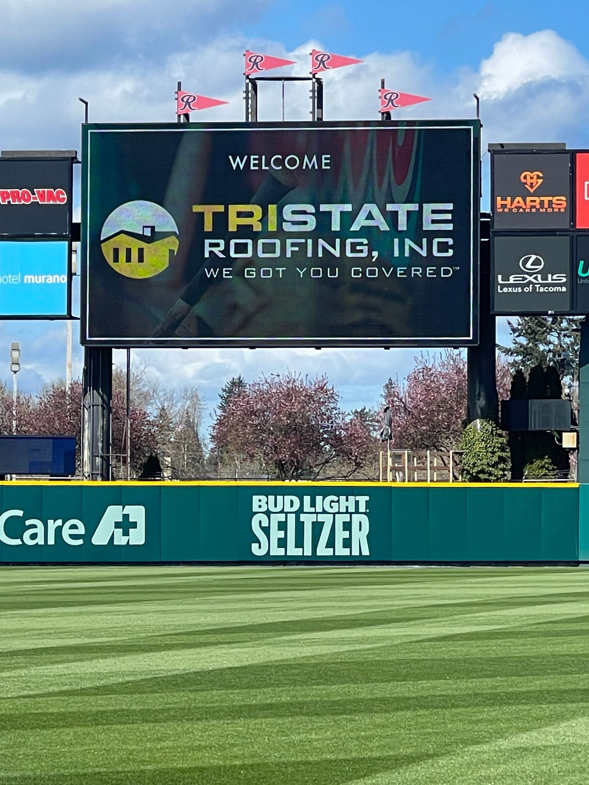 A large billboard on top of a baseball field advertising tristate roofing inc.