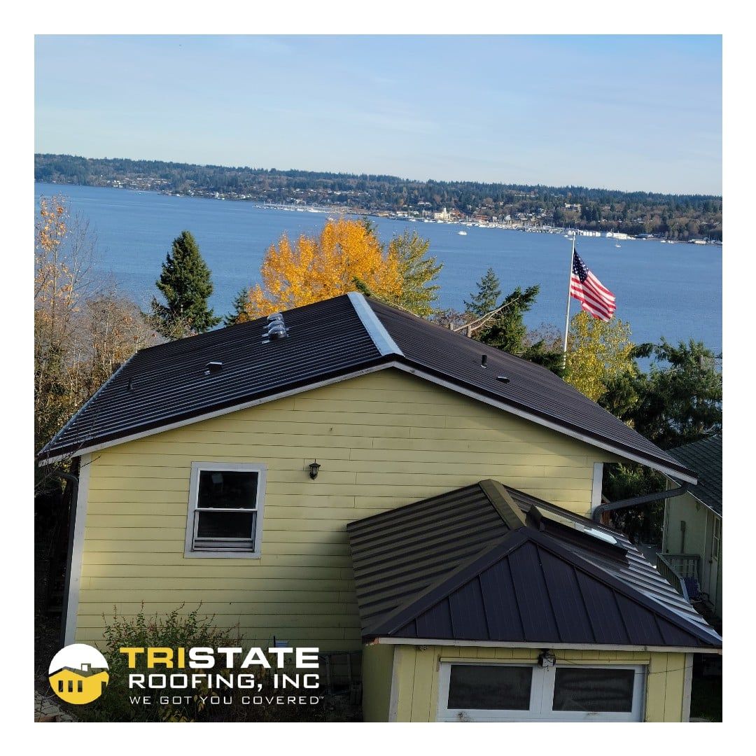 A yellow house with a black roof by tristate roofing inc