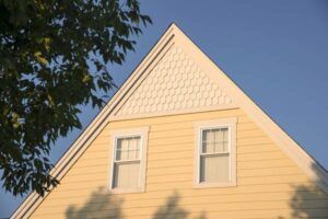 A yellow house with a triangle roof and two windows.