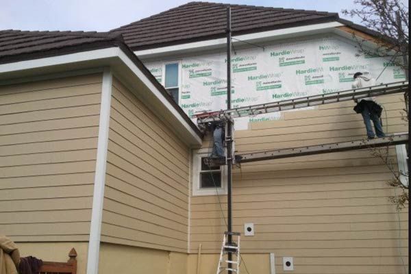 A man on a ladder is painting the side of a house
