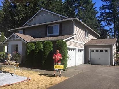 A man is standing in front of a house holding a sign.