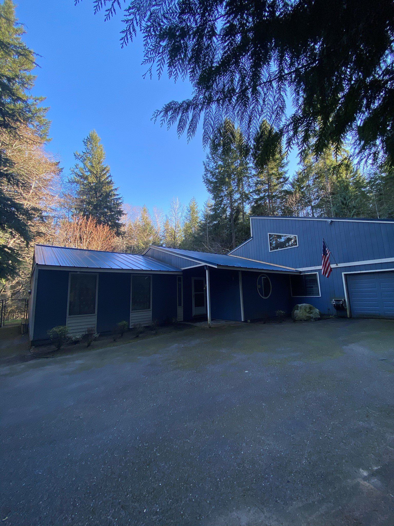 A blue house with a roof that is covered in solar panels is surrounded by trees.