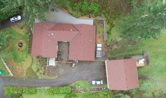 An aerial view of a house with a red roof in the middle of a forest.