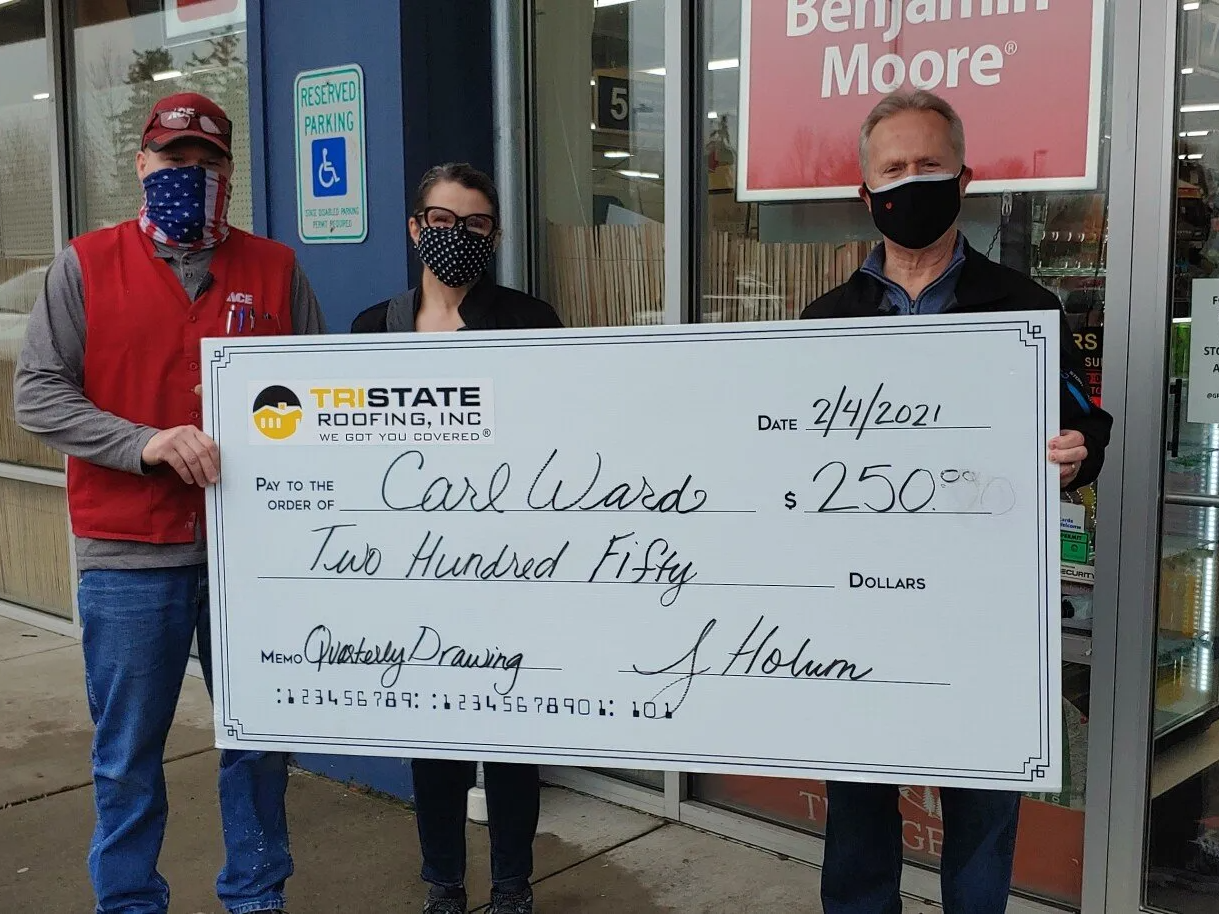 Three people wearing masks are holding a large check in front of a store.