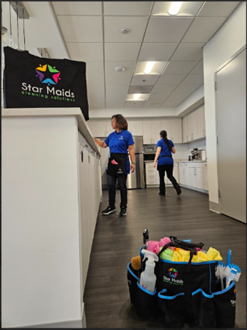 Two cleaners in blue uniforms work in an office kitchen, with branded Star Maids supply bags in the foreground.