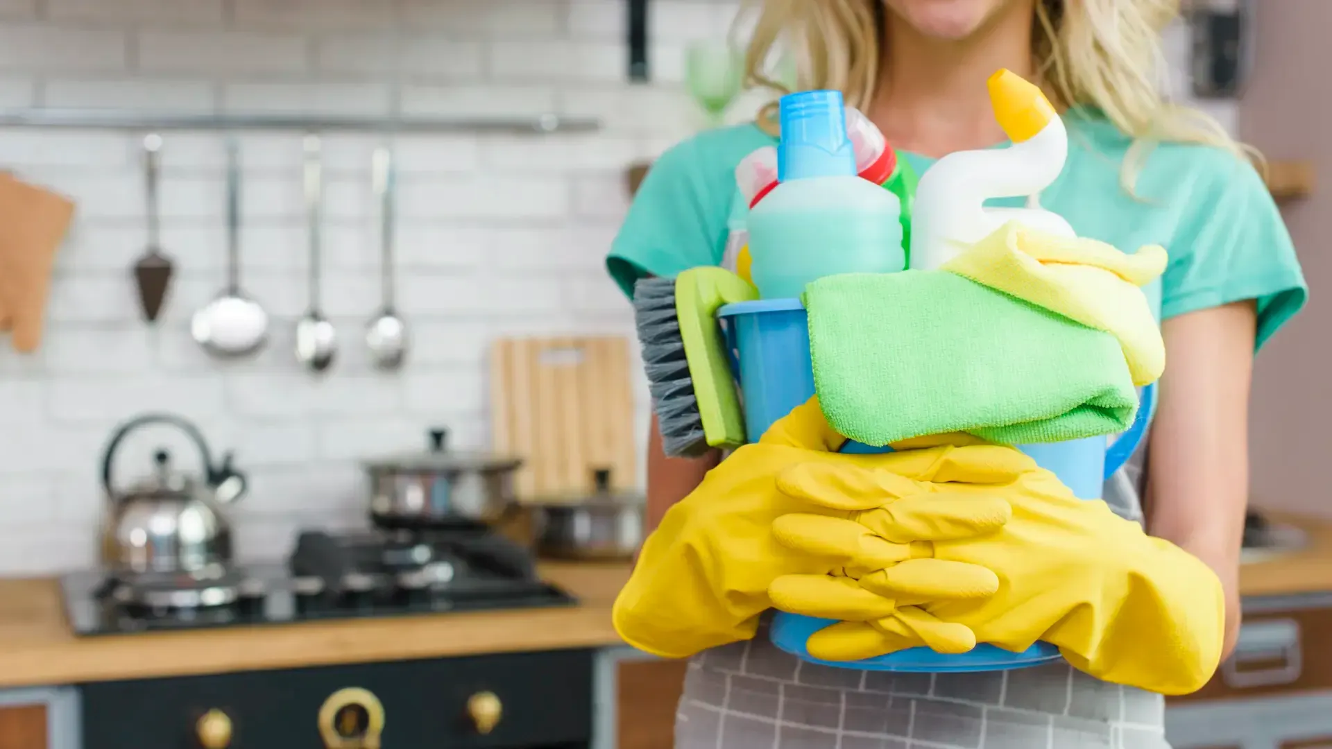Smiling woman holding cleaning supplies in kitchen
