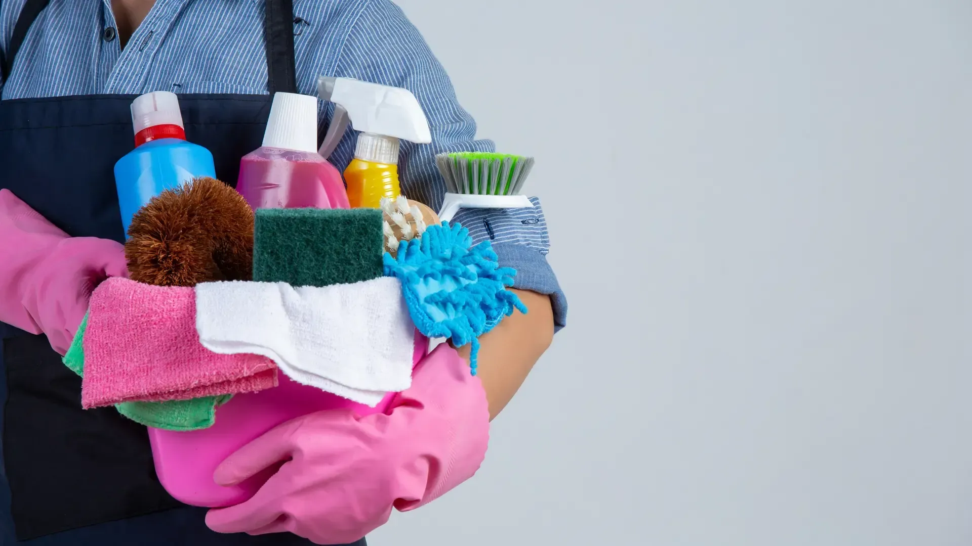 Woman in apron holding cleaning supplies and gloves