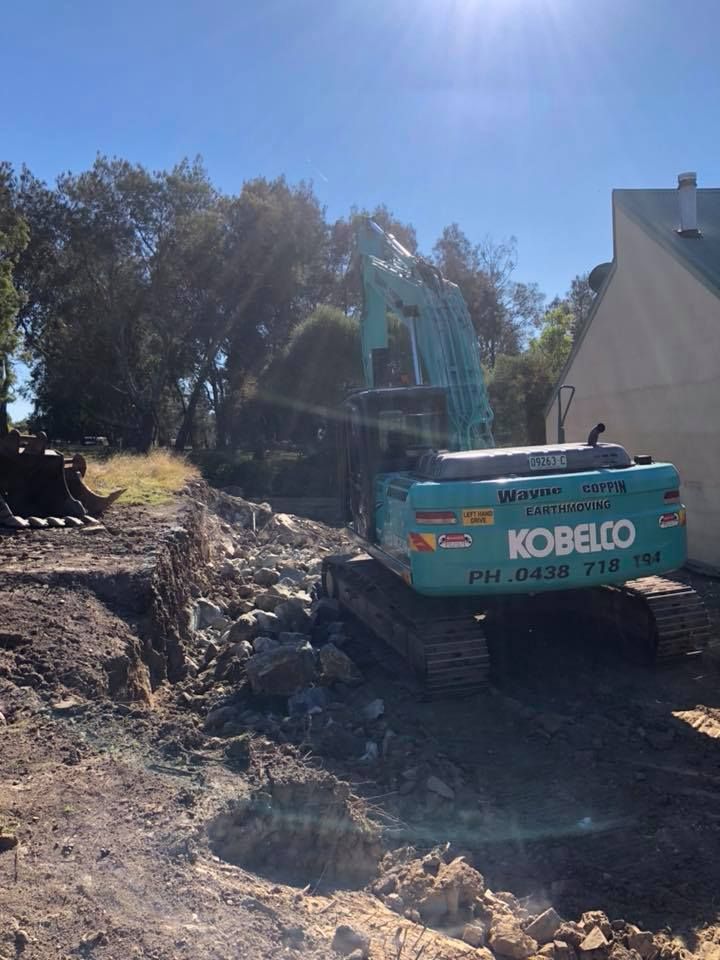 A kobelco excavator is sitting in the dirt in front of a house.