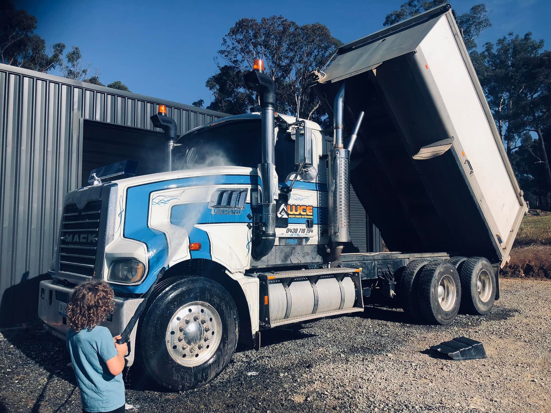 A boy is standing next to a dump truck with the number 5 on it.