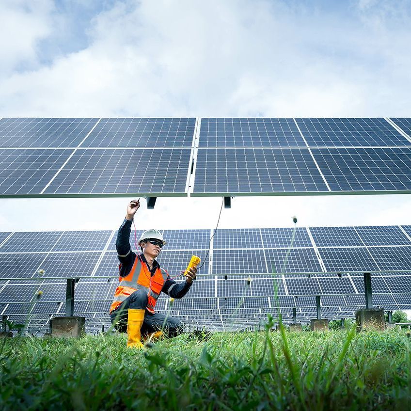 A man is kneeling in the grass in front of a solar panel.