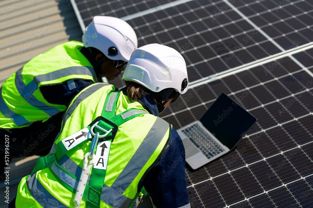 Two men are working on a solar panel and looking at a laptop.