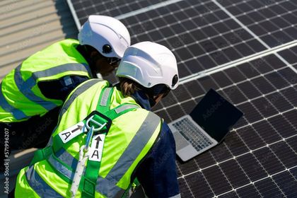 Two men are working on a solar panel and looking at a laptop.