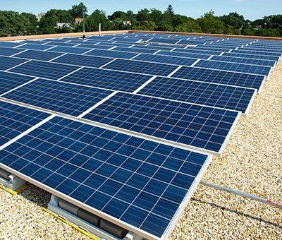 A row of solar panels on a roof with trees in the background