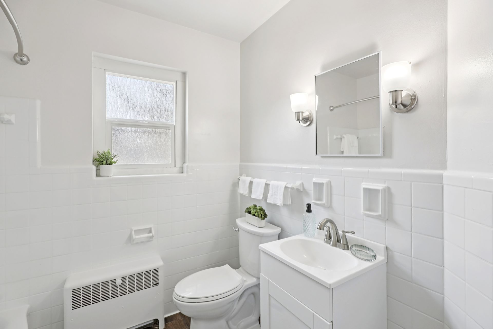 White bathroom with a window, sink, toilet, and mirror.