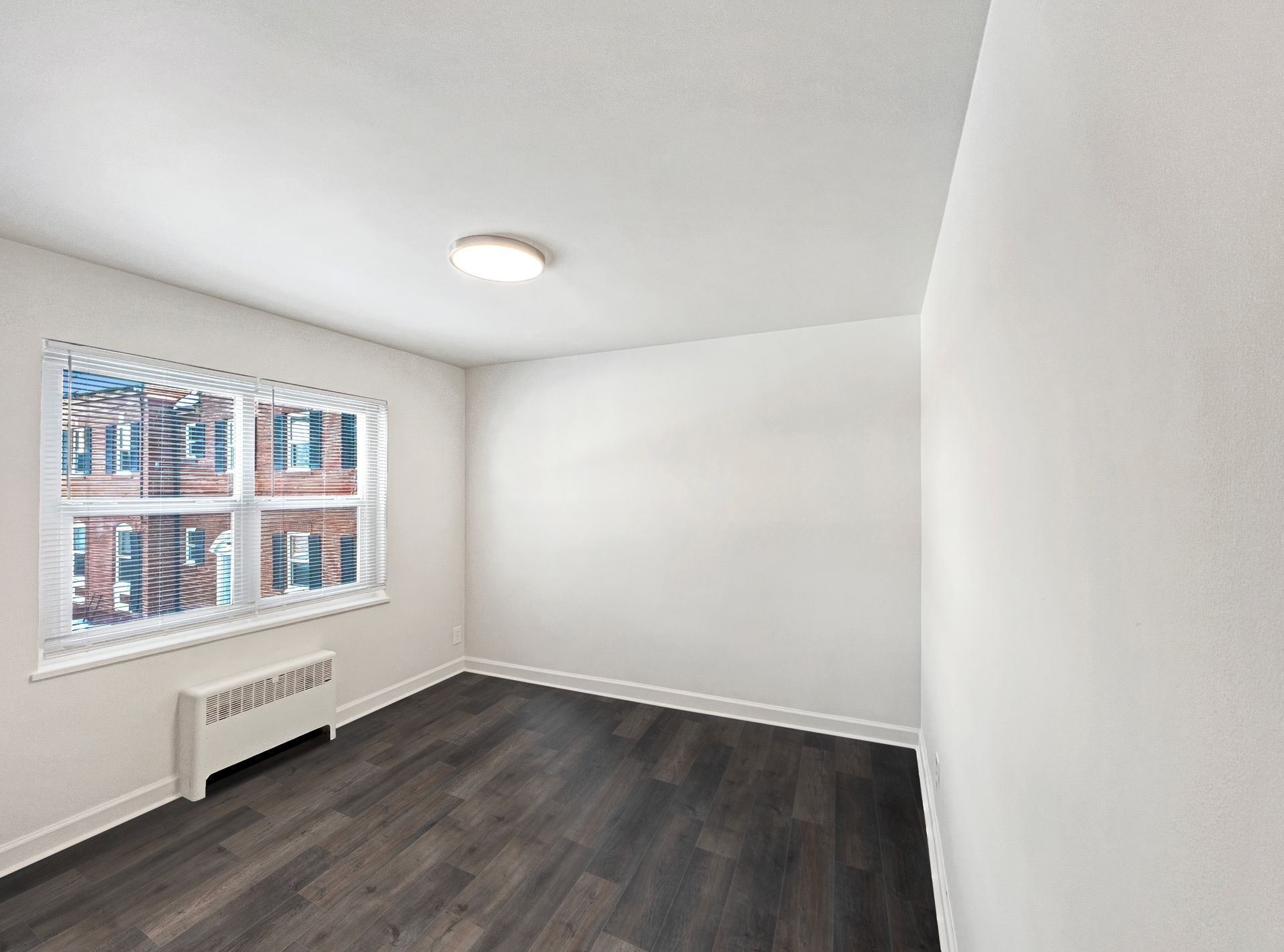 Empty room with dark wood floor, white walls, window, and radiator.