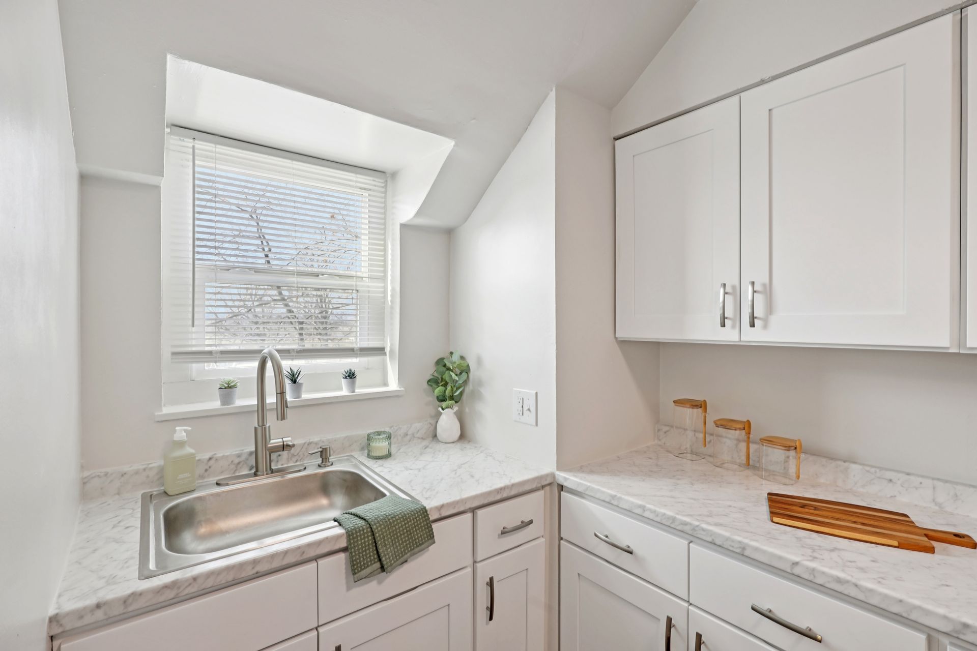 Kitchen with white cabinets, stainless steel sink, countertop, and window.