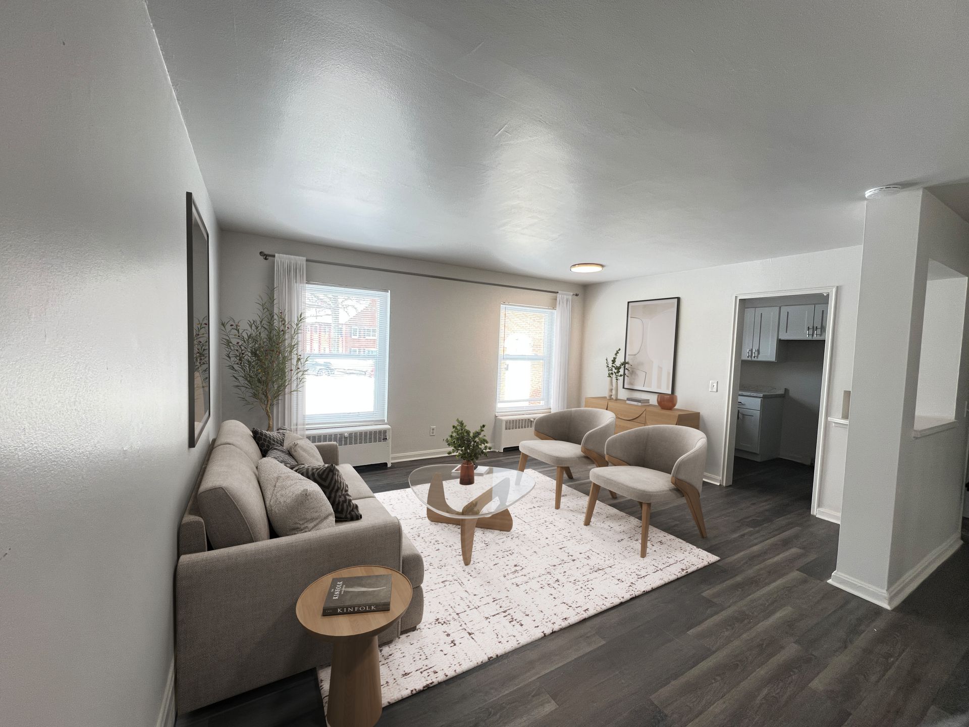 Living room with gray sofa, white rug, and two chairs. Dark wood floors, white walls, and bright windows.