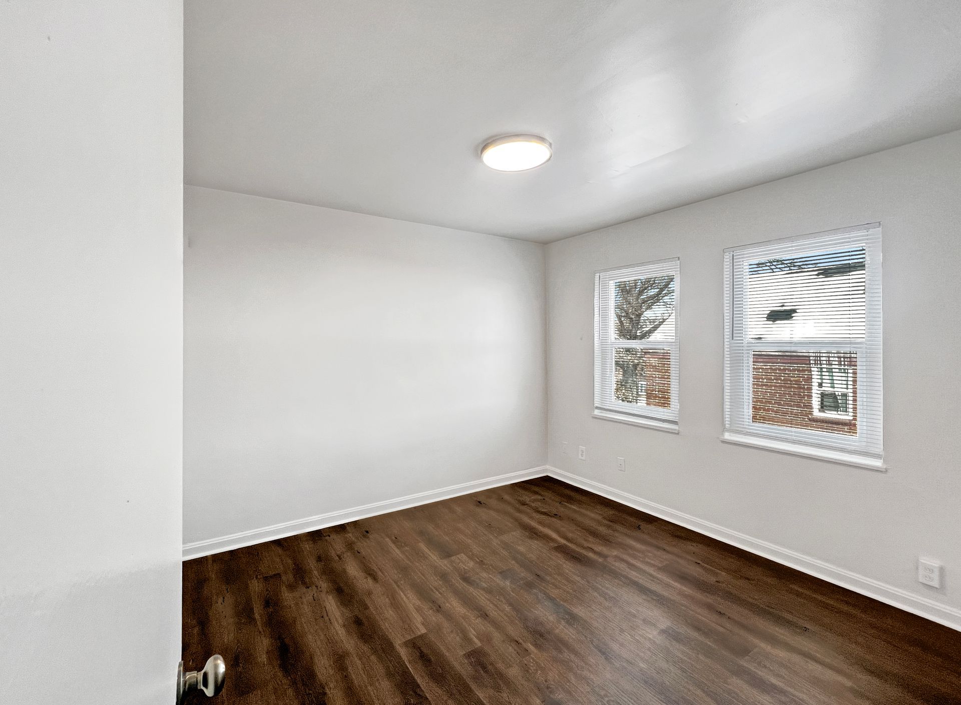 Empty room with hardwood floors, white walls, two windows, and a ceiling light.