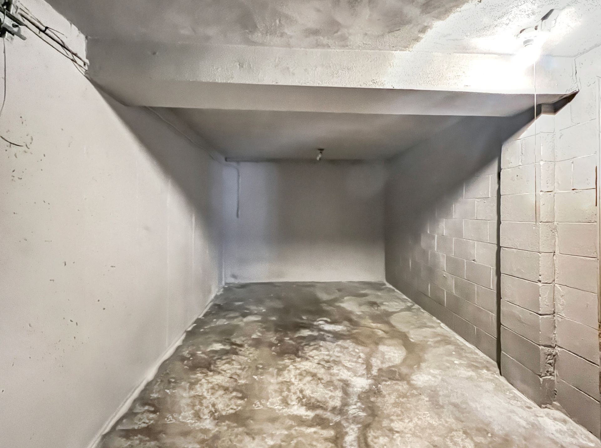 Empty concrete room, gray walls and floor, overhead beam, single light fixture.