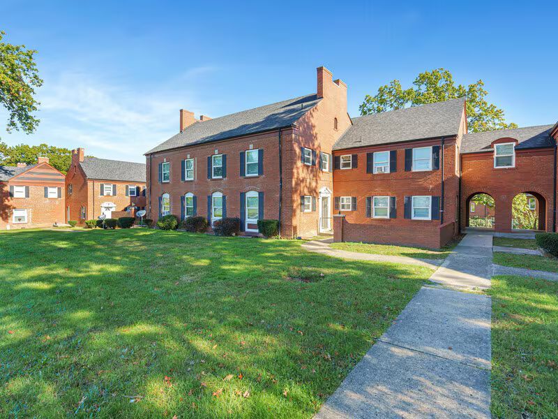 Brick apartment buildings with dark shutters, green lawn, and blue sky.