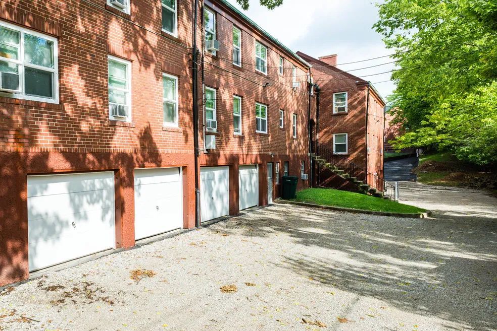 Brick apartment building with white garage doors and a sloping driveway.