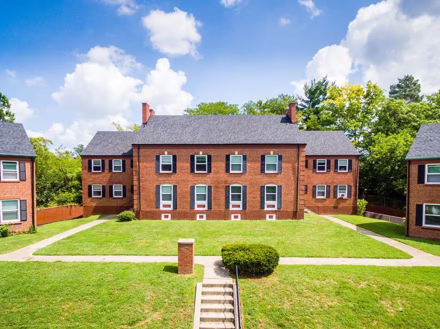 Brick apartment buildings with symmetrical windows, set on green lawns under a blue sky.