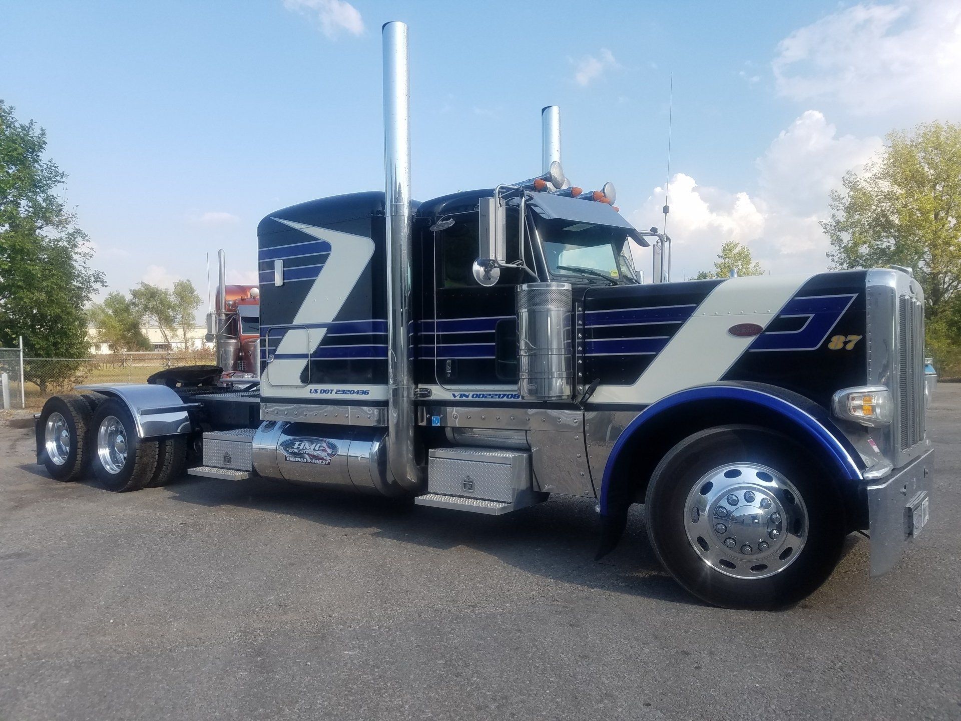 Black and white semi-truck with blue accents parked on pavement, under a blue sky.