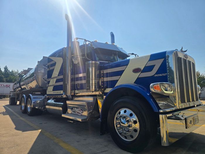 Blue and white semi-truck with chrome accents parked under a bright sun, likely a gas hauler.