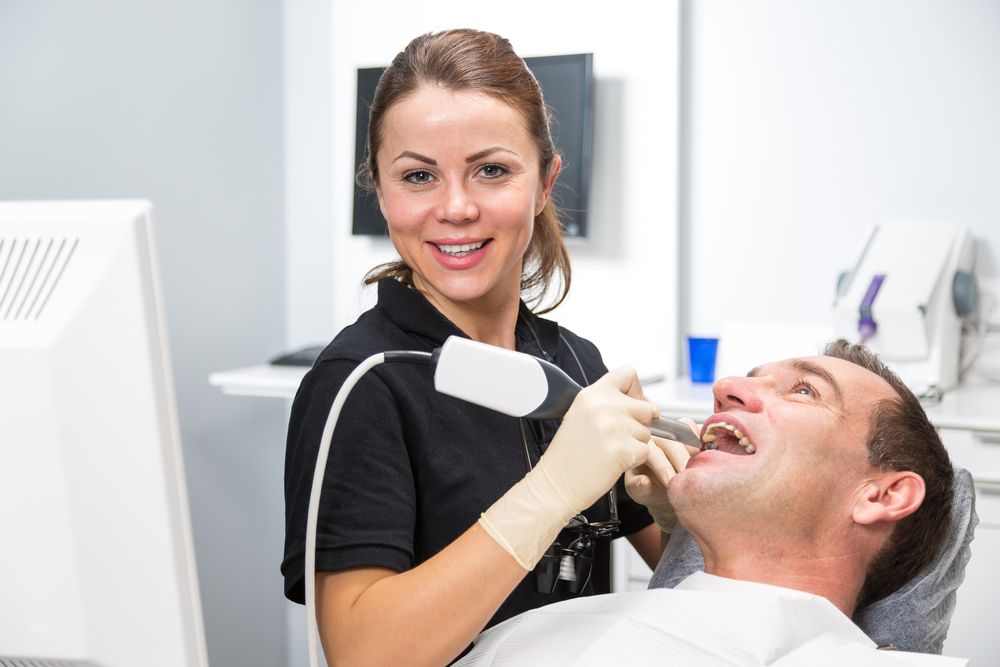 A female dentist is examining a man 's teeth in a dental office.