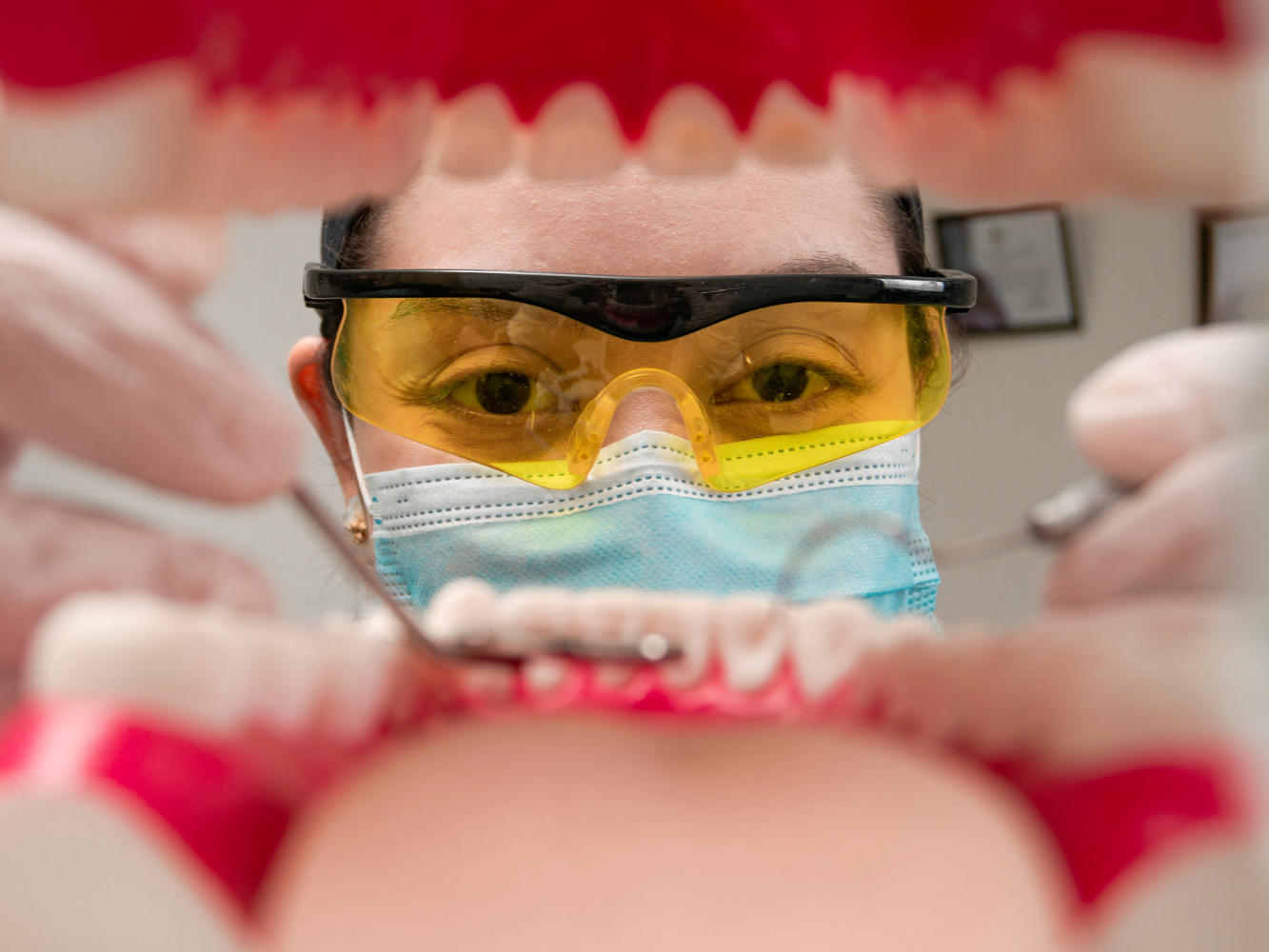 Dentist in protective gear examines teeth with tools inside a mouth model.