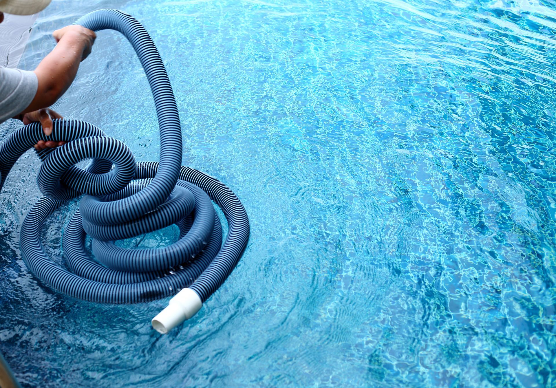 Pool technician holding vacuum hose over clean blue pool water.
