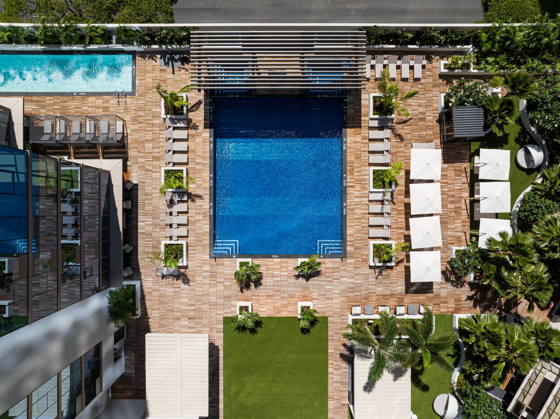 Overhead view of a rooftop pool area. Bright blue water, lounge chairs, and greenery.