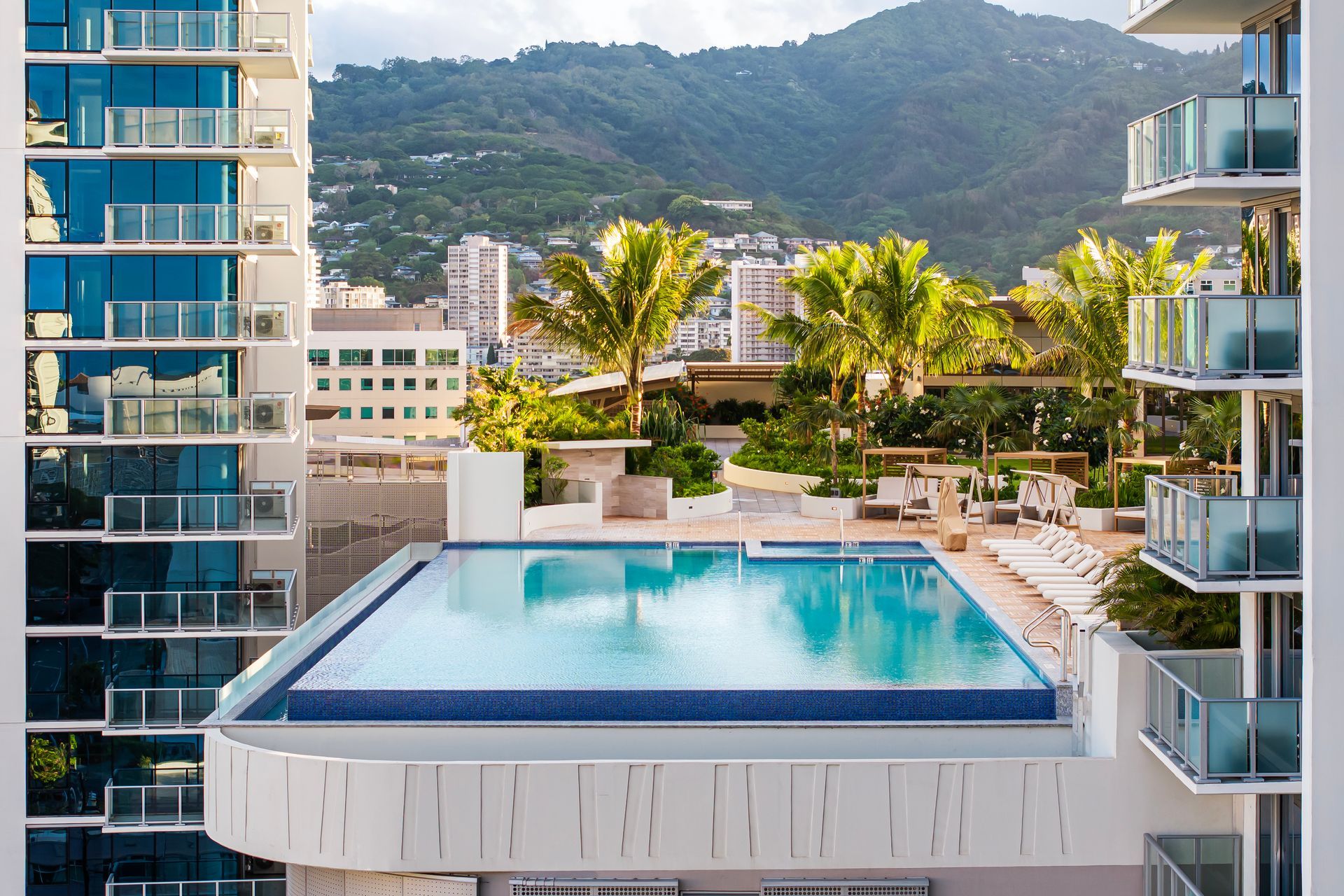 Rooftop pool surrounded by high-rise buildings, with city and mountain views.