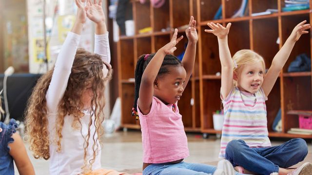 A group of young girls are sitting on the floor with their hands in the air.