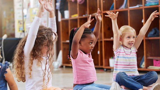 A group of young girls are sitting on the floor with their hands in the air.