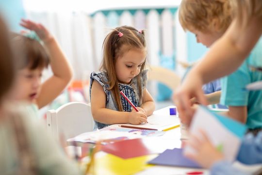 A group of children are sitting at a table drawing with markers.