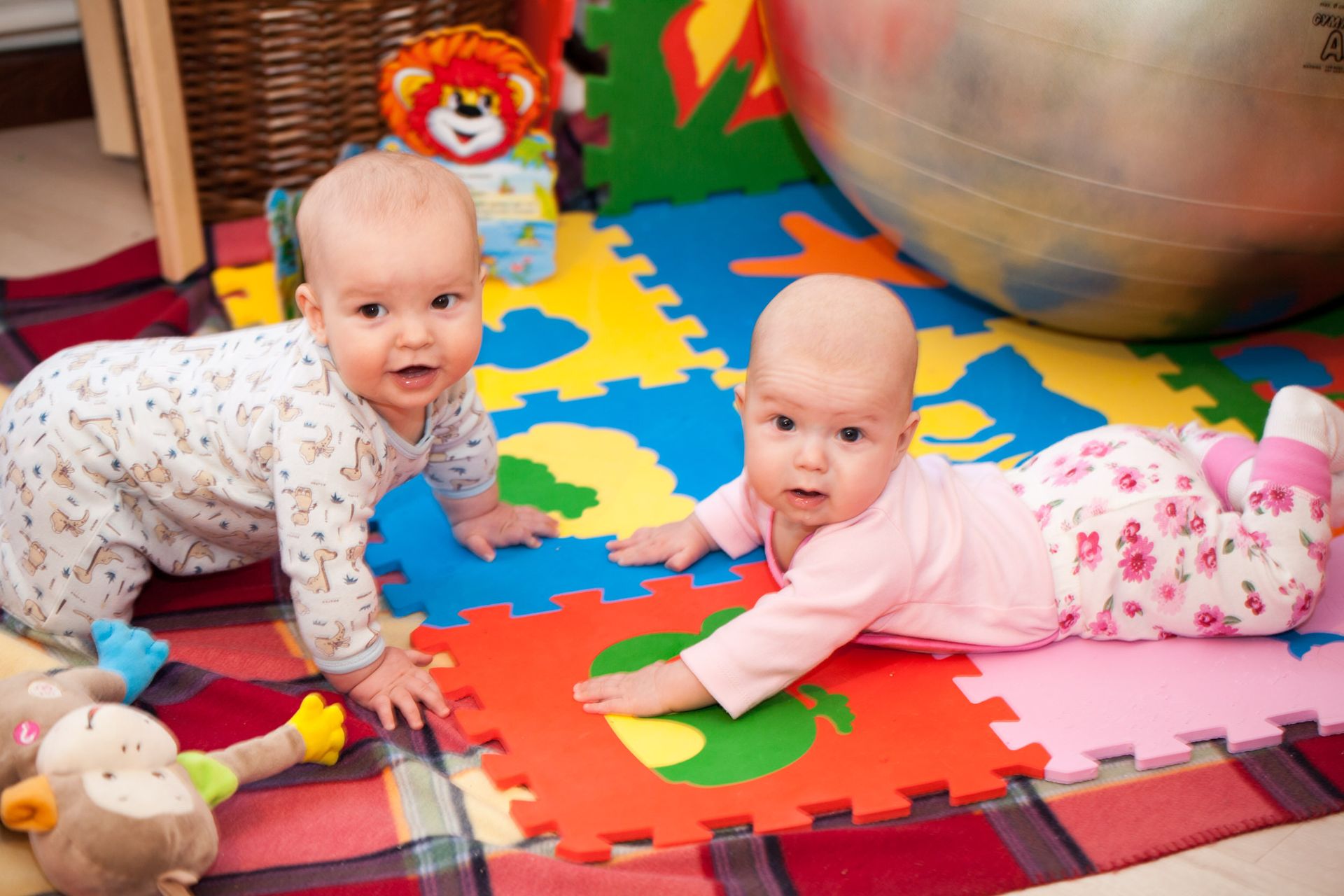 Two babies are crawling on a puzzle mat on the floor.