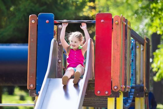 A little girl is sliding down a slide at a playground.