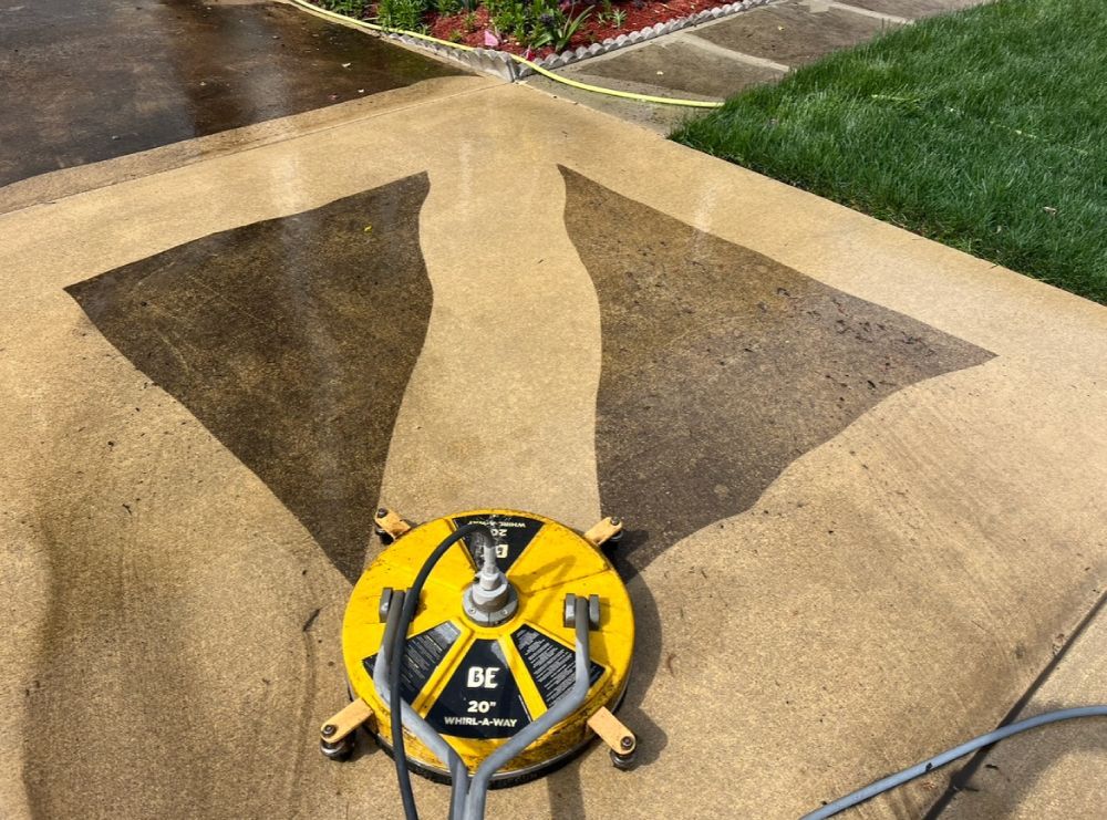 A yellow power washer cleaning a concrete surface, leaving a lighter path on the pavement.