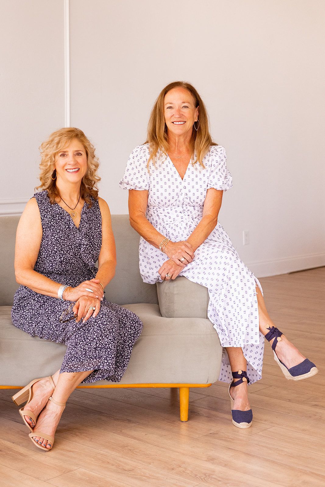 Two women standing by doorway; floral dress, green dress; smiles.