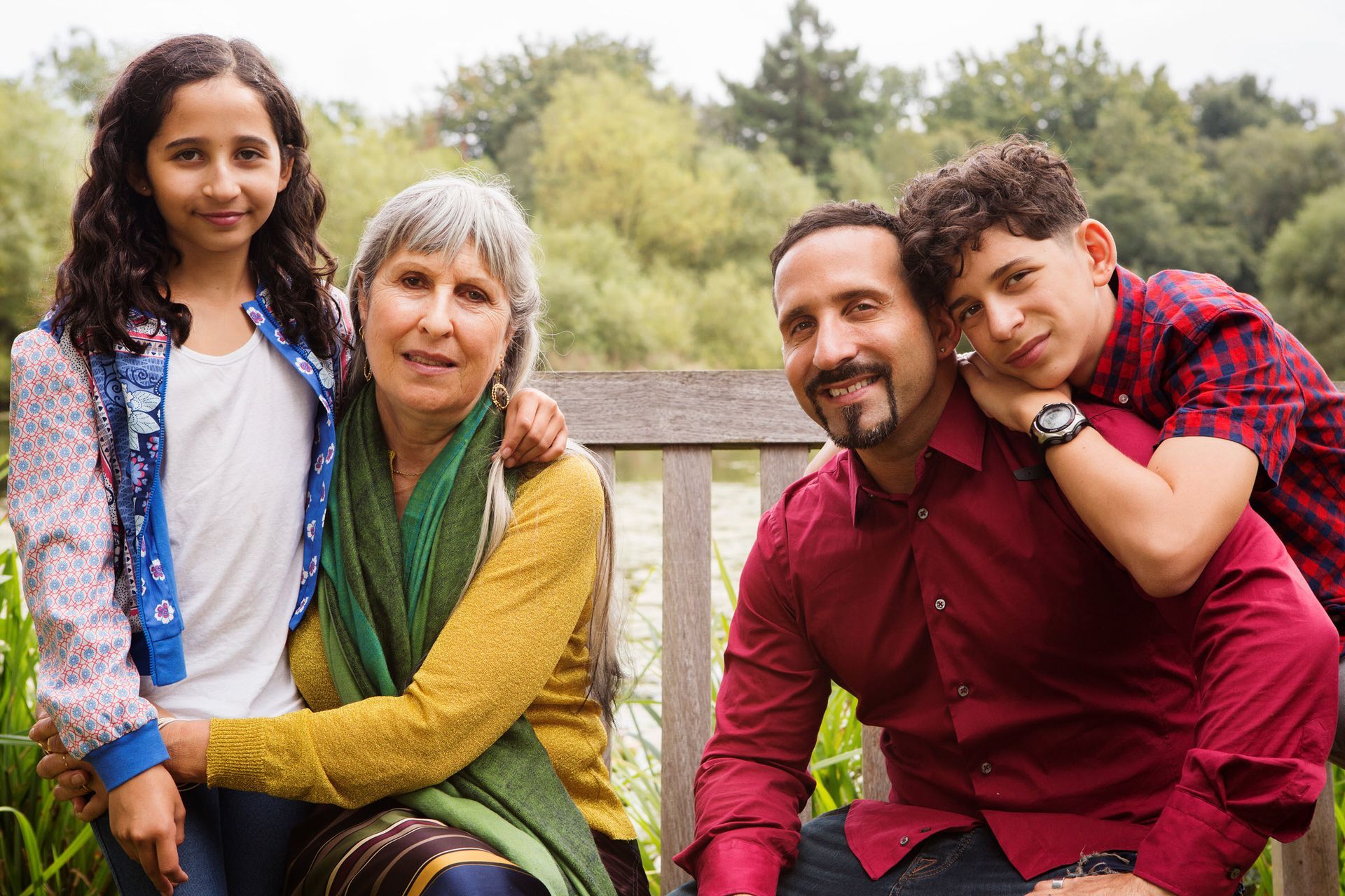 Family of four poses on a bench outdoors; the smiling adults have their arms around the children.