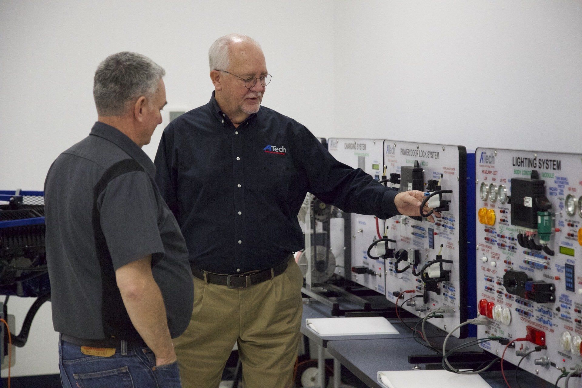 Two men are standing next to each other in front of a forklift simulator
