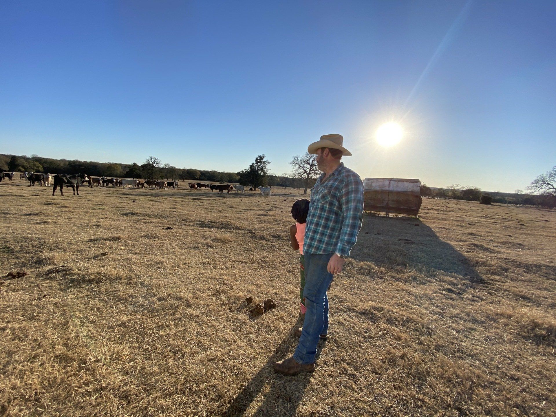 A man in a cowboy hat is standing in a dry grassy field.