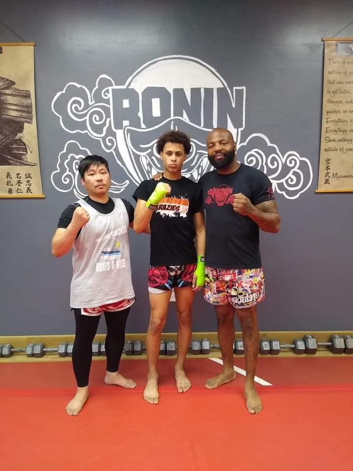 Three men are posing for a picture in front of a sign that says ronin.
