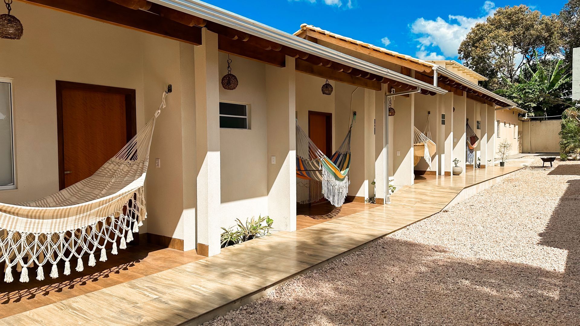 Fileira de prédios brancos com portas marrons e redes penduradas, dia ensolarado.