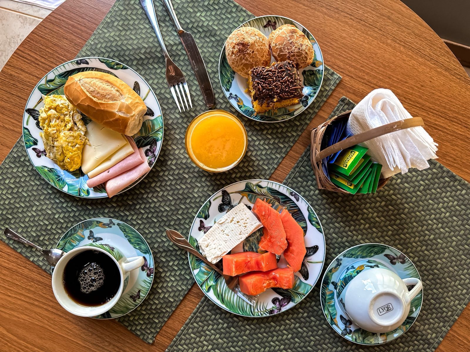 Café da manhã: pratos de comida, café, suco de laranja e guardanapos sobre a mesa.