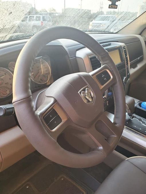 Brown steering wheel of a Dodge Ram truck with control buttons and logo visible inside the cabin.